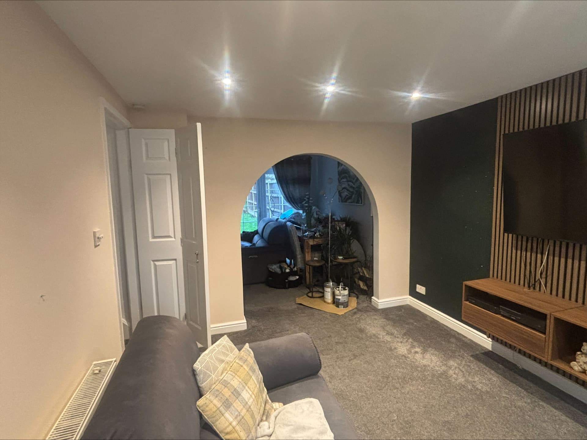 Lounge with deep forest green painted media wall behind oak slat panelling and warm neutral walls