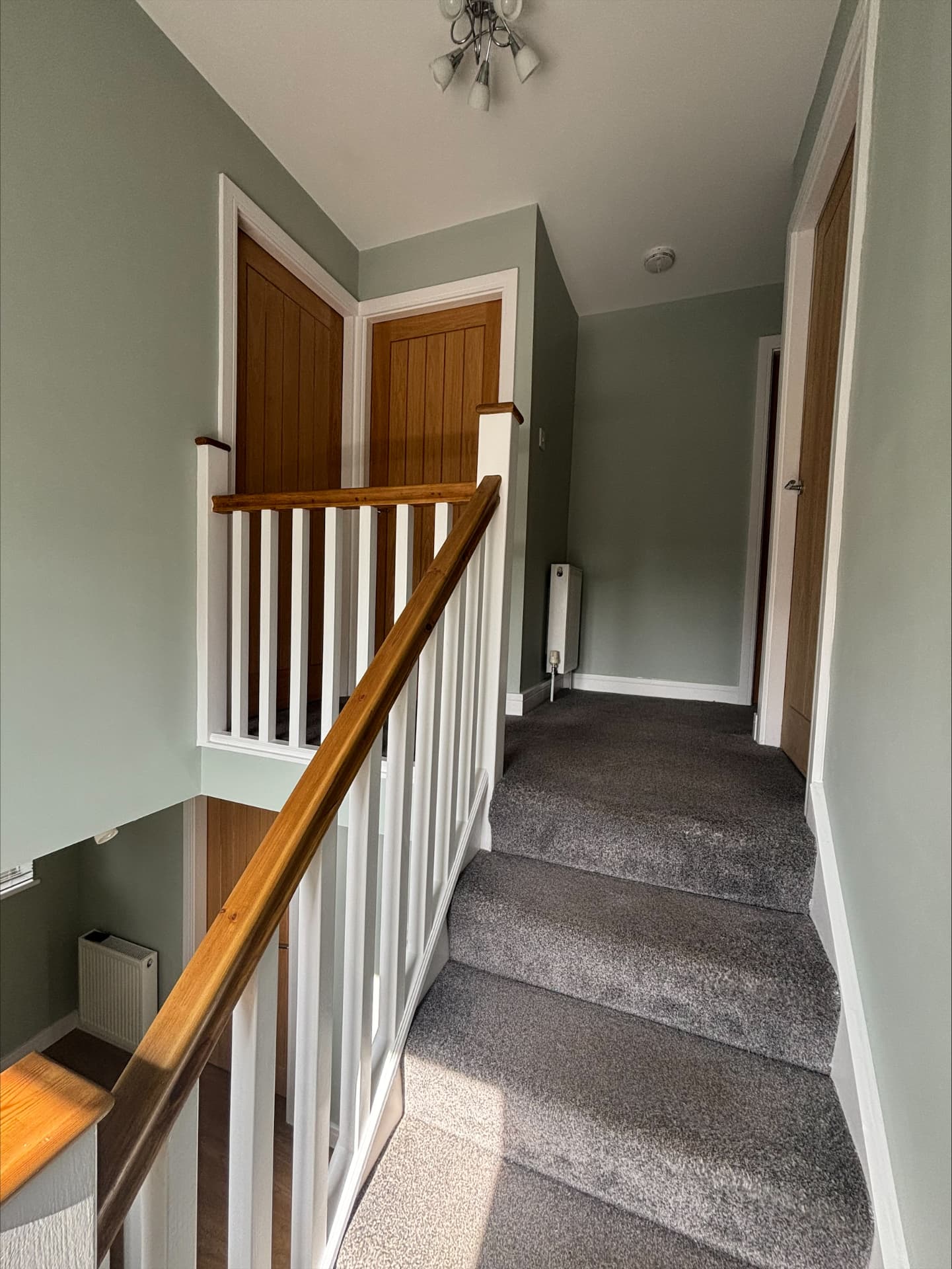 Sage green landing and stairs with oak handrail, oak doors and hand-painted white spindles