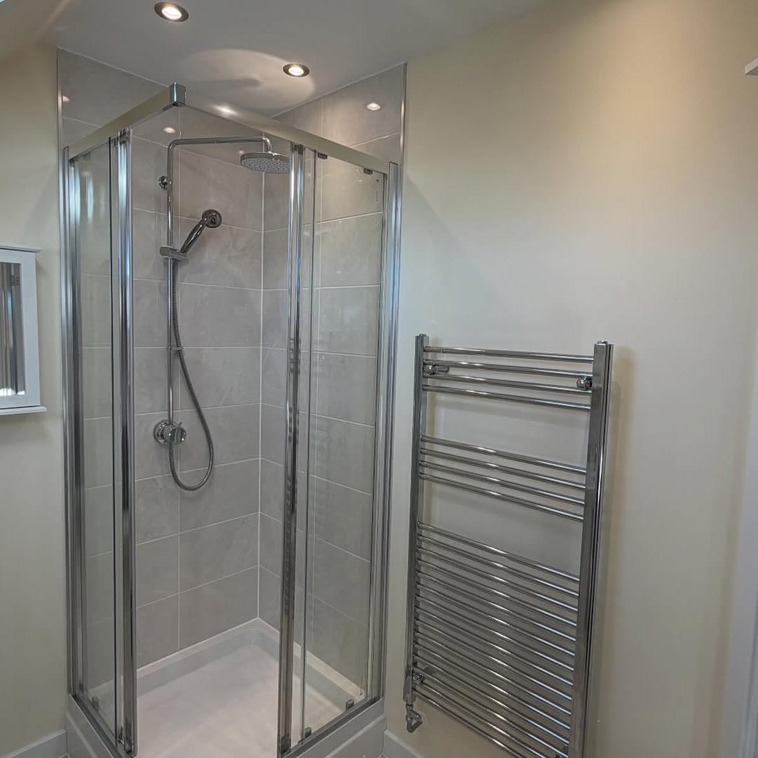 Glass shower enclosure and chrome towel rail against freshly painted walls