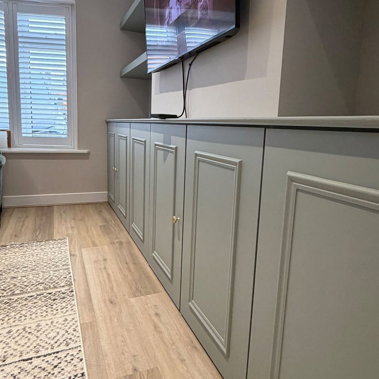 Bespoke built-in cupboards hand-painted in soft grey along a living room wall