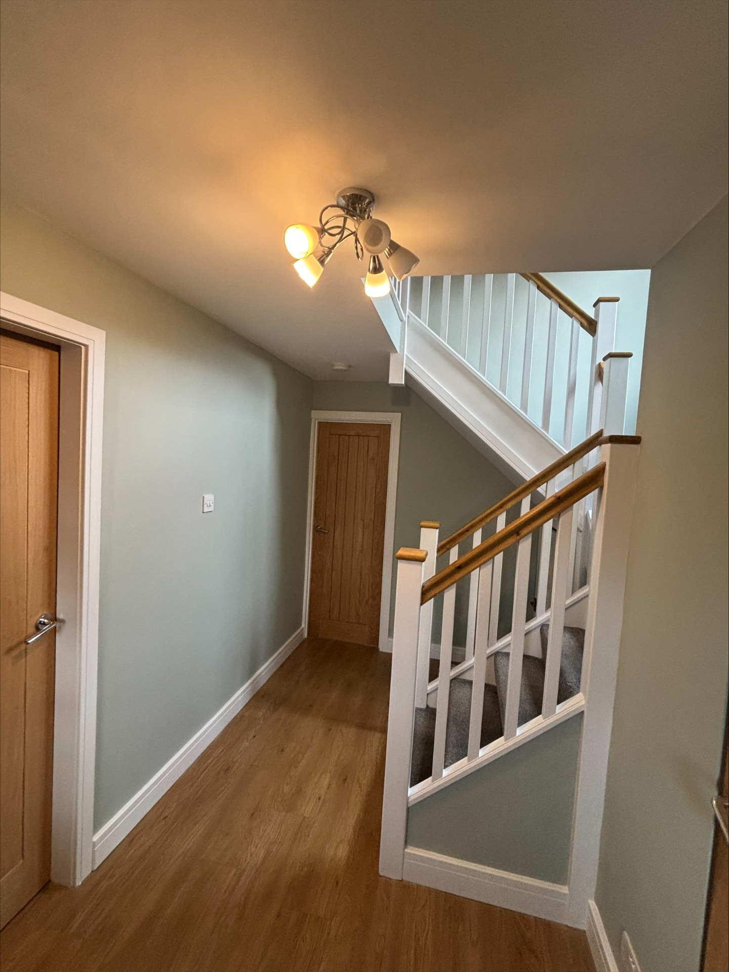 Sage green hallway with crisp white woodwork, oak doors and painted staircase balustrade