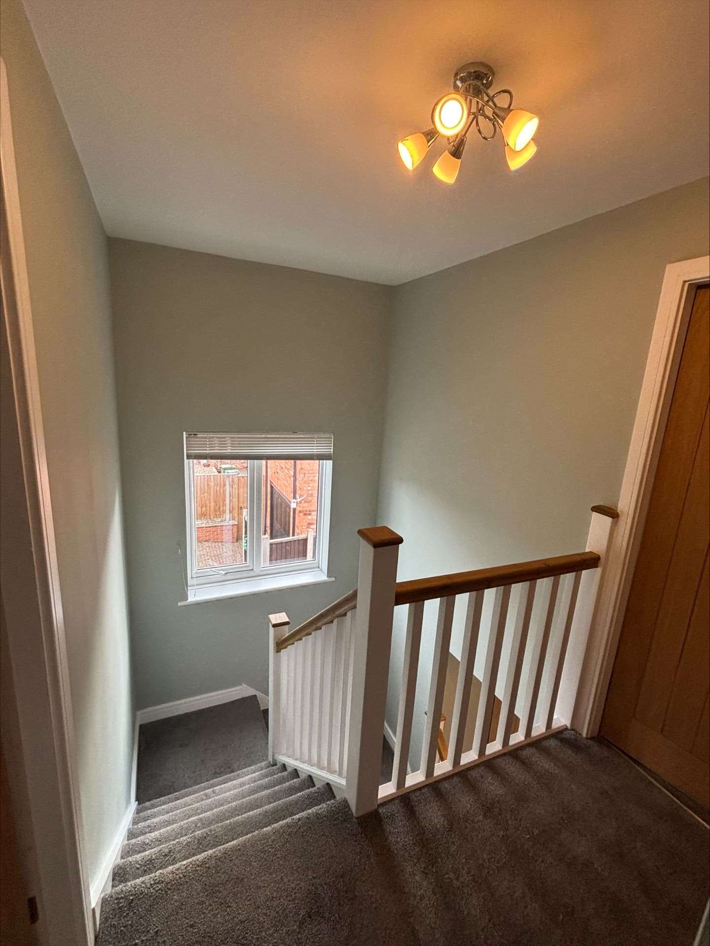 Sage green stairwell with white skirtings, landing window and oak-capped balustrade