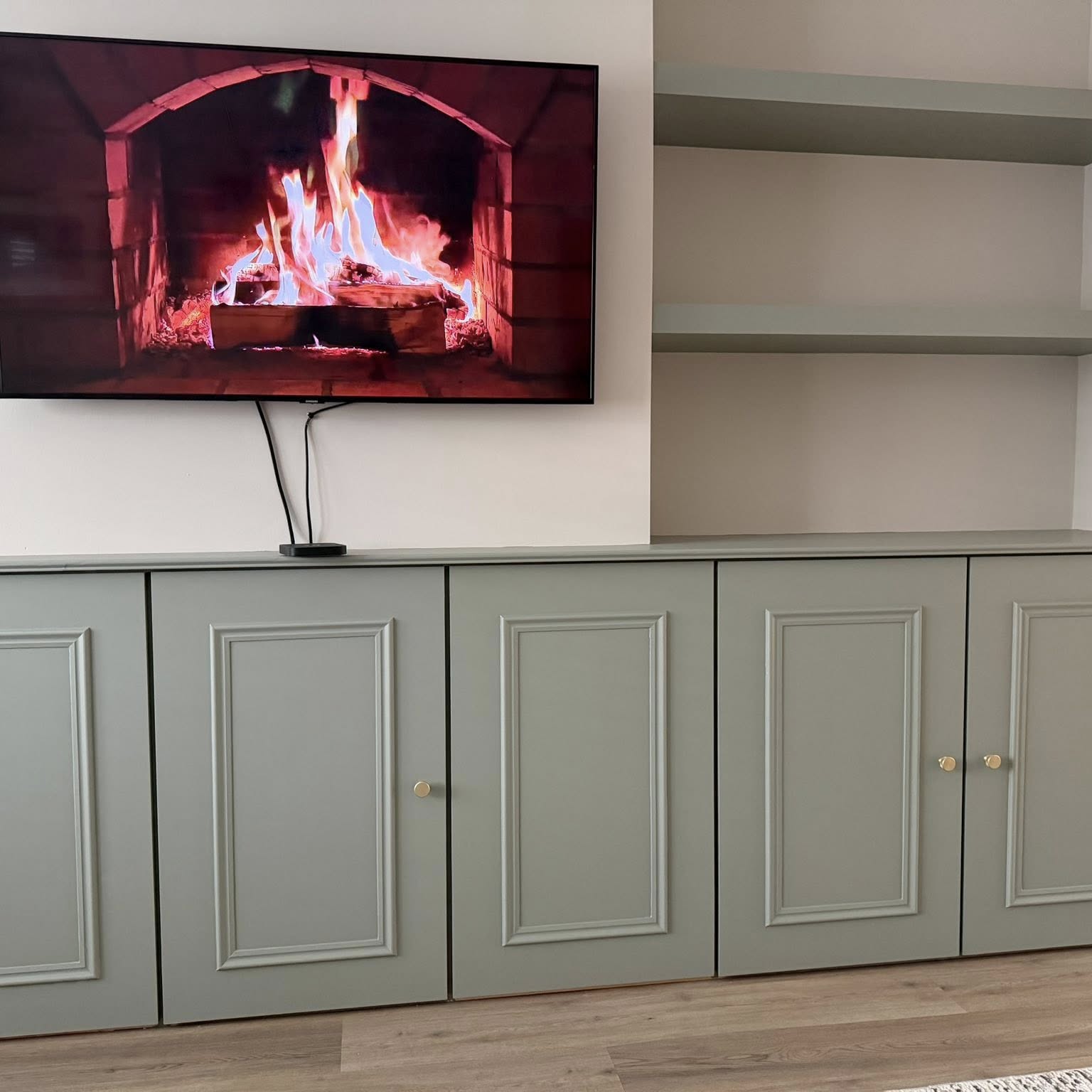 Hand-painted sage media unit with floating shelves around a wall-mounted fireplace