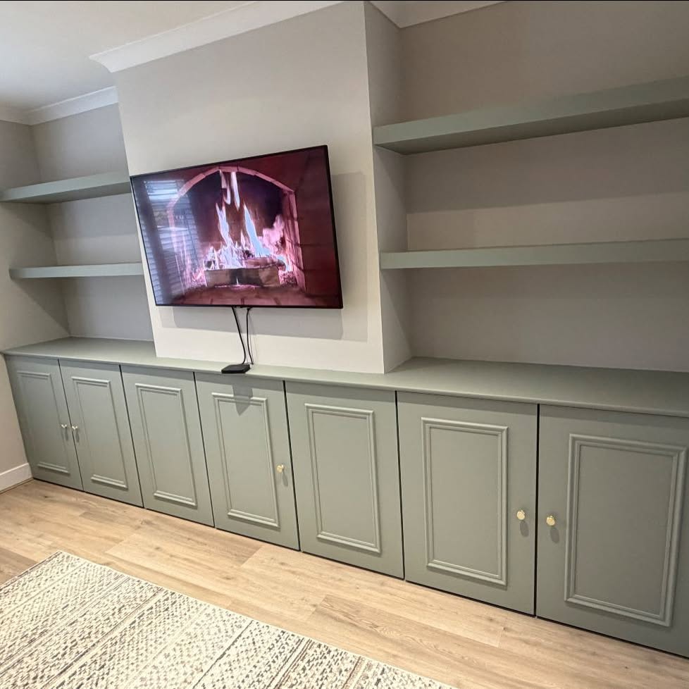 Hand-painted sage green media wall with floating shelves and panelled cupboards in a Worcestershire living room