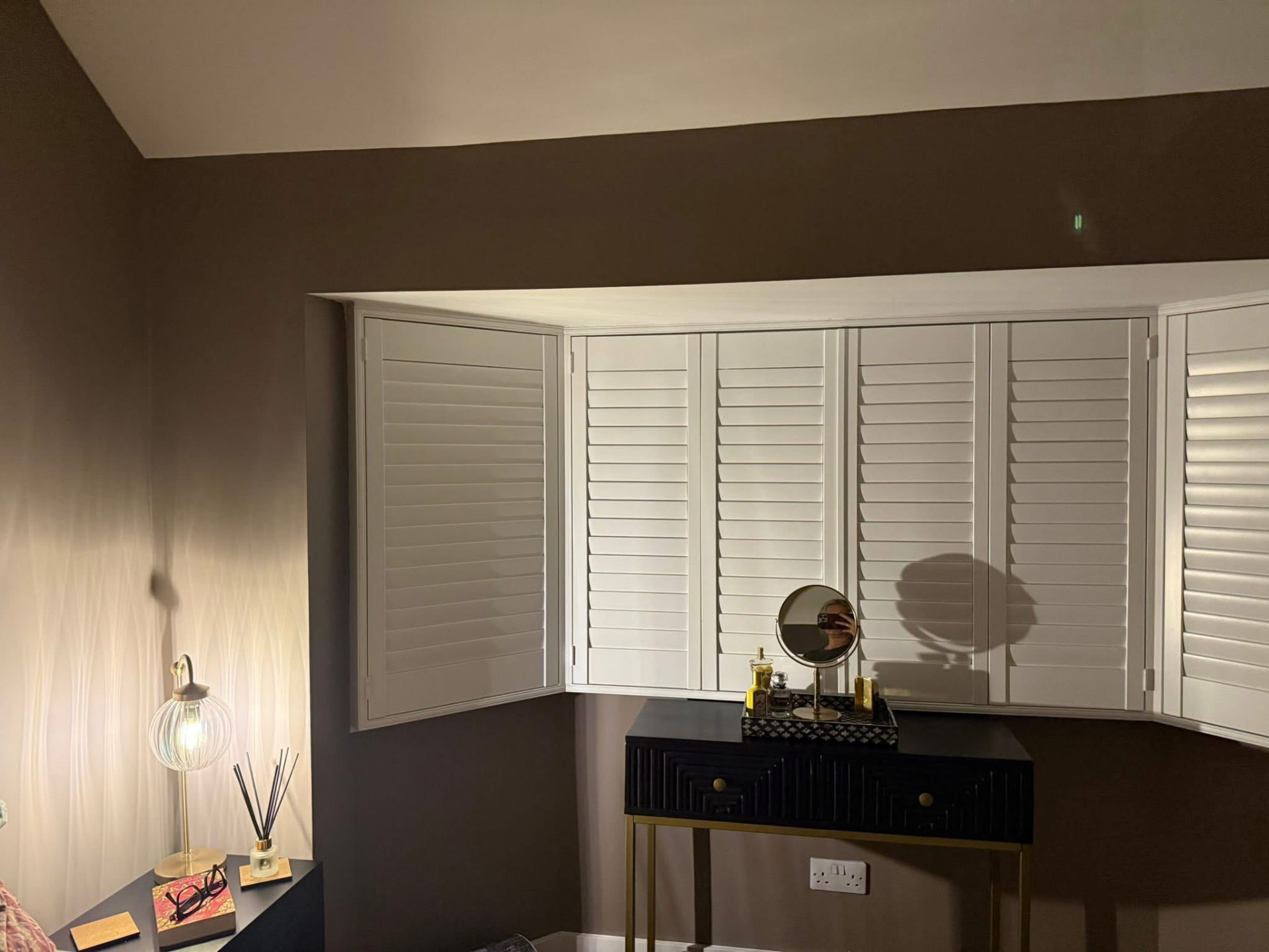 Bedroom bay window with white plantation shutters framed by deep chocolate painted walls