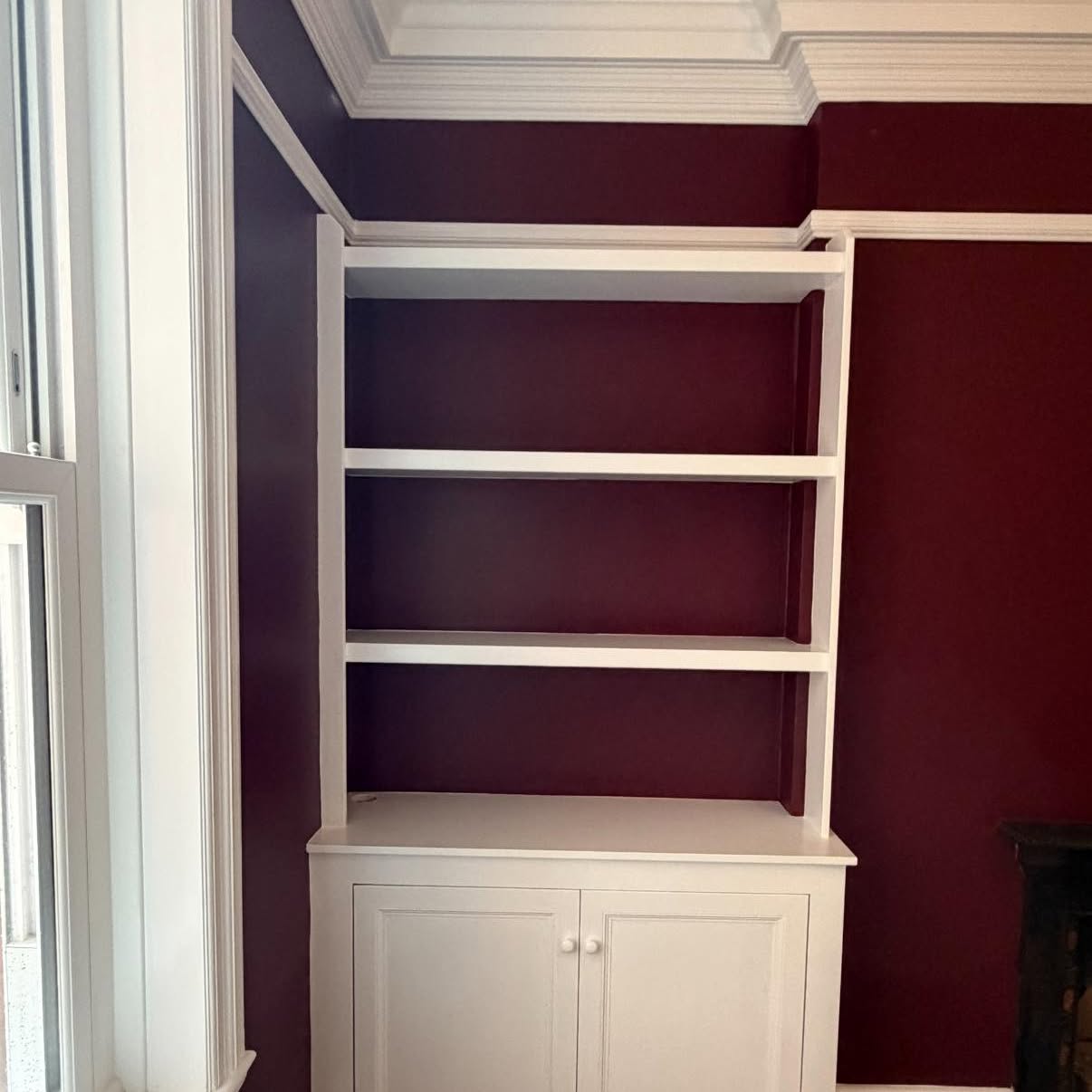 Alcove shelving and cupboard hand-painted white against deep burgundy walls