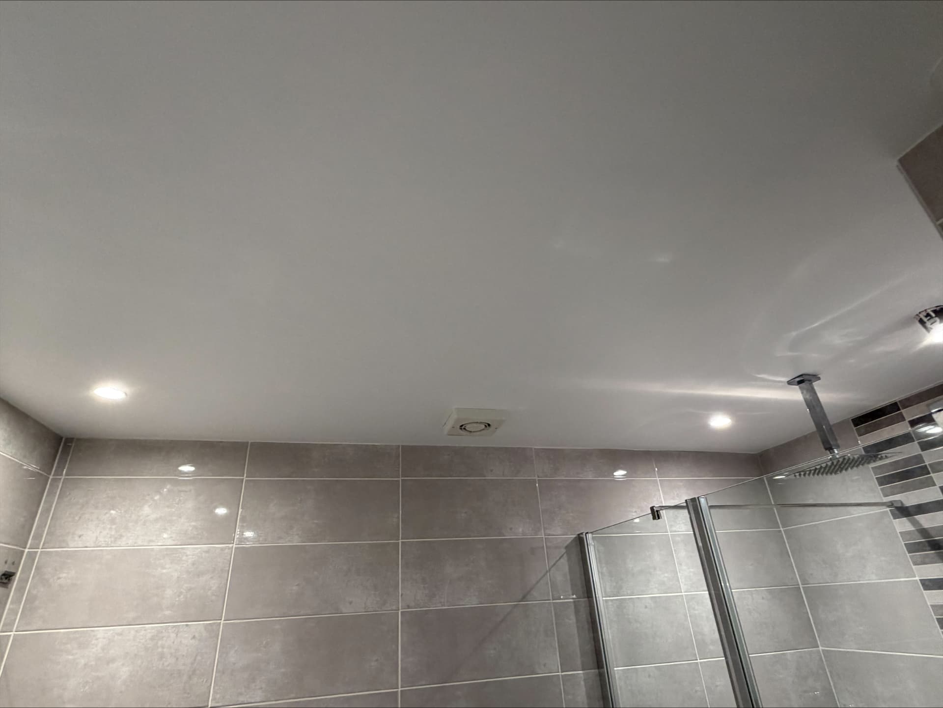 Shower room ceiling painted in a flawless white finish above grey stone-effect tiling