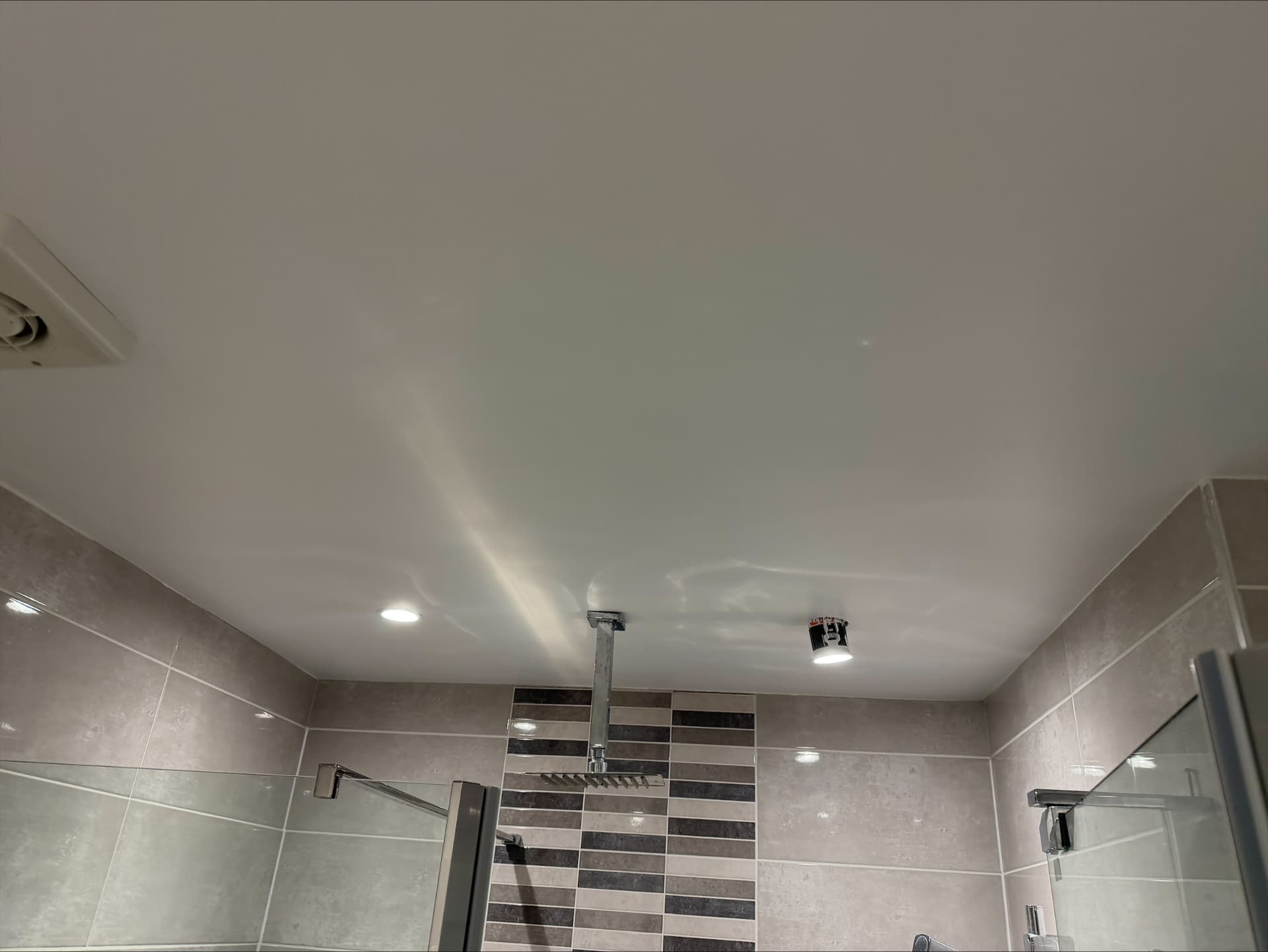 Freshly painted moisture-resistant bathroom ceiling cut in cleanly to stone tiling above a rainfall shower
