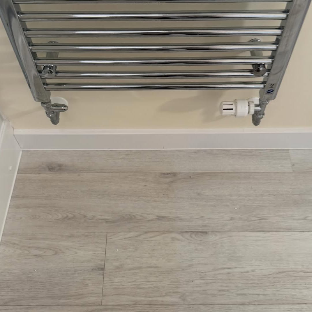 Chrome towel radiator above pale wood-effect flooring in a refreshed bathroom