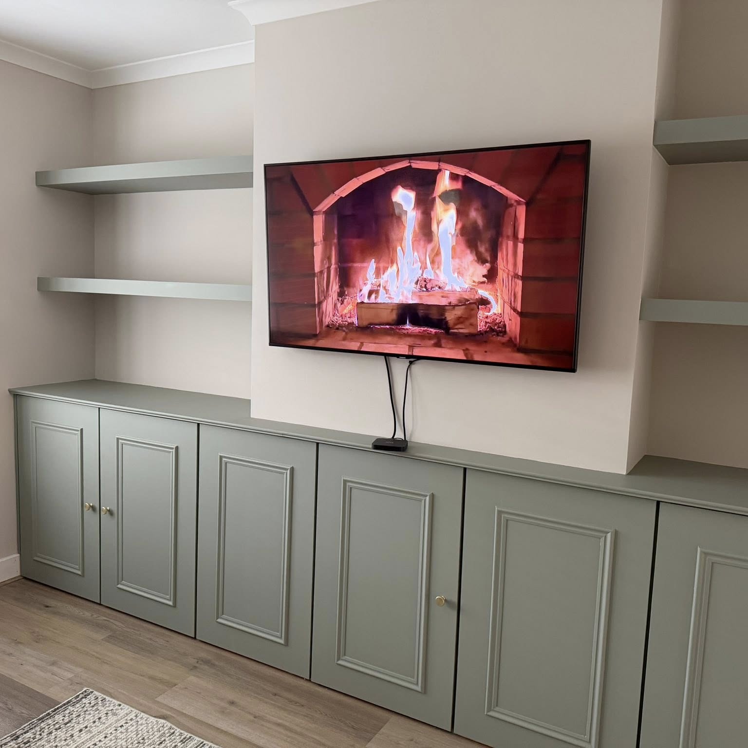 Full-width hand-painted sage cabinetry with floating shelves and wall-mounted media unit