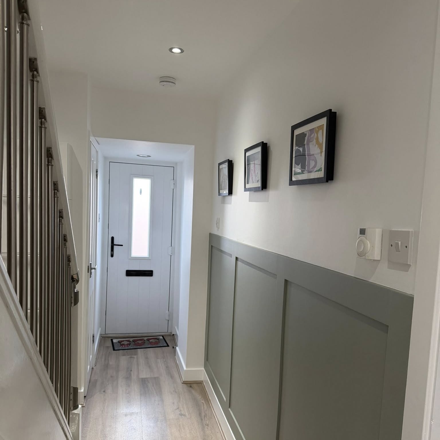 Freshly painted hallway with sage panelled wainscoting, white walls and framed artwork